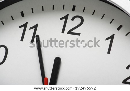 Close up of a simple clock face with the hour and minute hands approaching midnight or twelve o\'clock