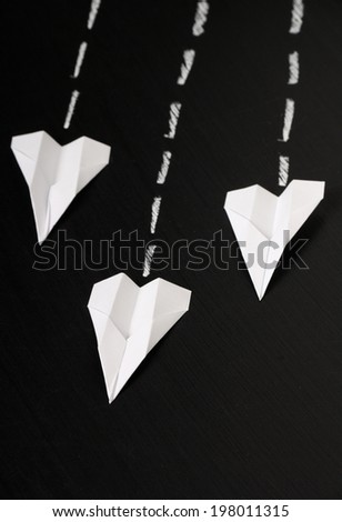 Three paper airplanes made from white paper fly in formation across a blackboard surface.