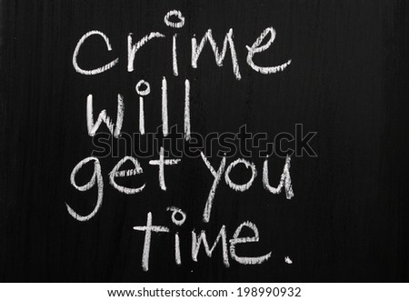 The phrase Crime Will Get You Time written by hand in white chalk on a used blackboard