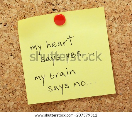 The phrase my heart says yes, my brain says no written on a yellow sticky note pinned to a cork notice board.
