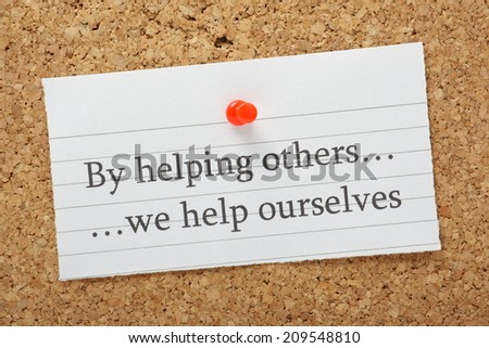 The phrase By helping others we help ourselves typed on a piece of lined paper pinned to a cork notice board
