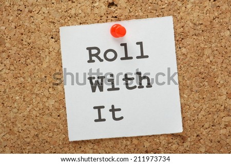 The phrase Roll With It on a piece of white paper pinned to a cork notice board. Another way of saying take it as it comes.