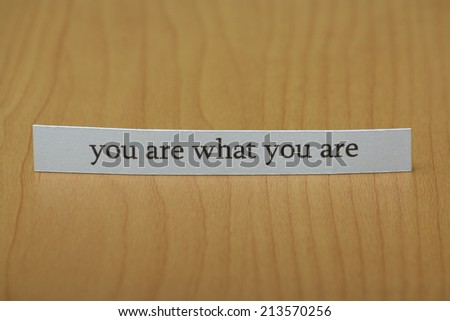 The phrase you are what you are typed on a strip of white paper and left standing on a wooden desktop surface