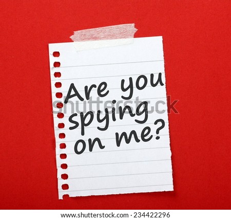 The question Are you spying on me? written on a scrap of lined paper and sticky taped to a red notice board