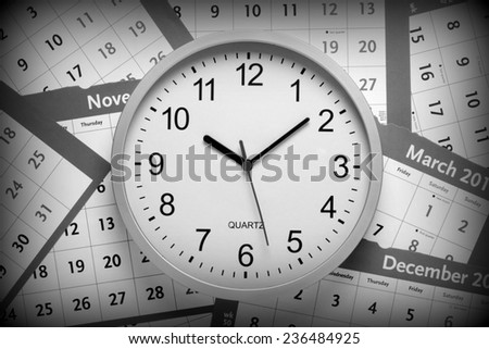 A black and white image of a modern office clock on a background of pages torn from a  wall calendar. A vignette has been added for effect.