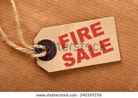 Paper luggage tag with string on a brown wrapping paper background with the text Fire Sale on the label