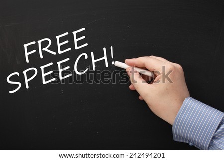Hand writing the phrase Free Speech on a blackboard using a stick of white chalk