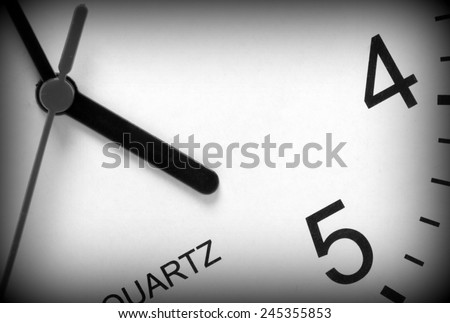 Close up of a modern clock face in black and white with the hour hand pointing at five o\'clock. A vignette has been added to the image for effect