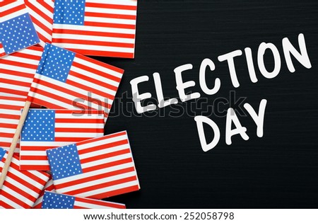 The phrase Election Day on a blackboard alongside miniature paper flags of the United States of America