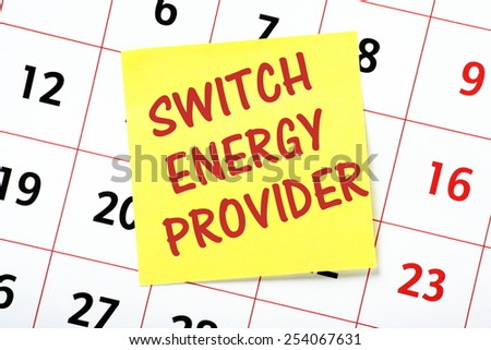 A reminder to Switch Energy Provider written in red ink on a yellow sticky note and pasted to a wall calendar