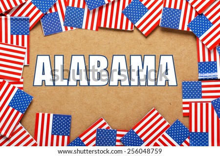 Miniature flags of the United States of America form a border on brown card around the name of the state of Alabama