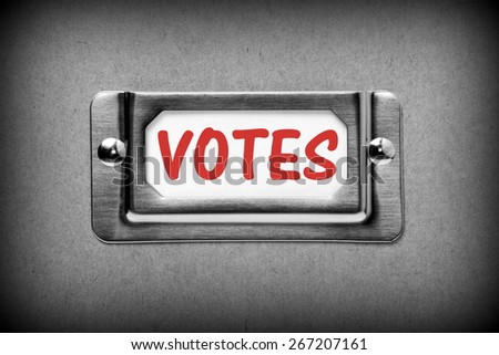 Black and white image of a desk drawer,cardboard box or storage container label with the word VOTES in red ink on a white index card