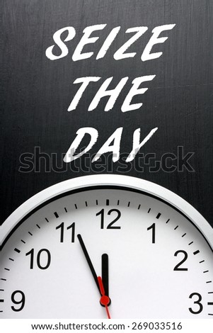 The phrase Seize The Day in white text on a blackboard next to a modern wall clock displaying the time at almost midnight