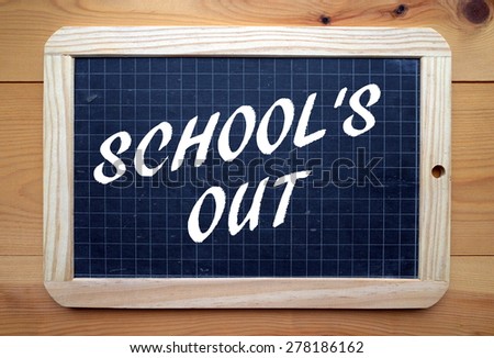 The phrase School\'s Out in white text on a slate blackboard placed on a wood surface