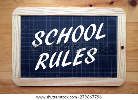 The phrase School Rules in white text on a slate blackboard placed on a wooden surface