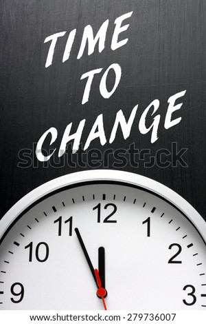 The phrase Time to Change in white ext on a blackboard above a modern wall clock with the hands pointing towards twelve