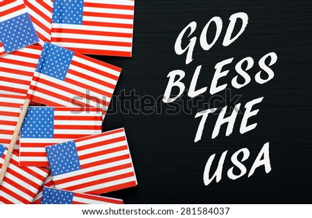 The phrase God Bless The USA on a blackboard next to miniature stars and stripes flags
