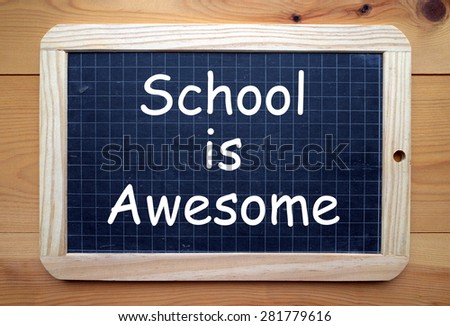 The phrase School Is Awesome in white text on a slate blackboard placed flat on a wooden surface