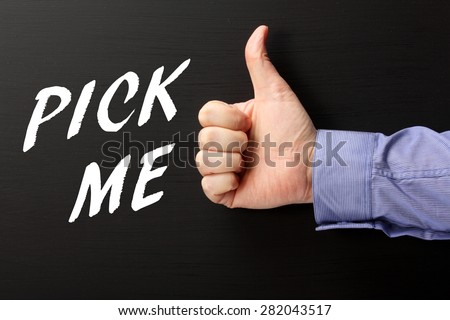 Male hand wearing a business shirt giving the thumbs up sign for the phrase Pick Me in white text on a blackboard