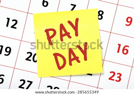 The phrase Pay Day in red text on a yellow sticky note posted on the page from a calendar as a reminder