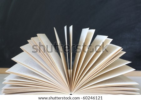 An open book with pages spread in front of an empty blackboard