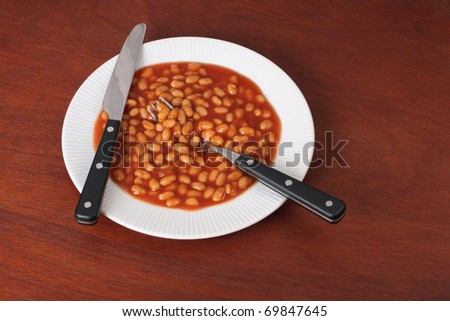 A cheap meal for hard times,baked beans on a plate with cutlery on a wood background
