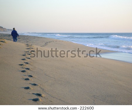 Man walking on beach with a trail of footprints