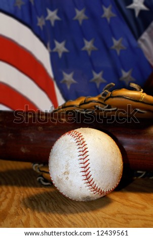 Well used baseball, bat and glove rest on a sheet of plywood with an American flag in the background.
