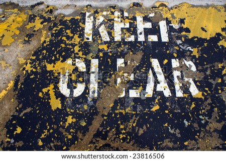 A keep clear stenciled on concrete is worn and grungy.