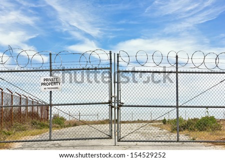 Private property sign hangs on a metal fence. Gate is locked close with a chain and several padlocks.