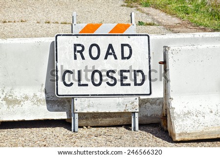 Road sign and concrete barriers are used to show road is closed.