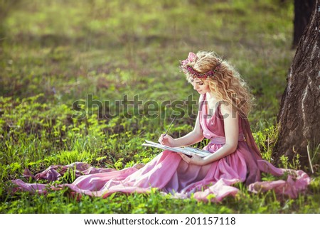 Girl in a fairy dress sitting under a tree in the woods and draws