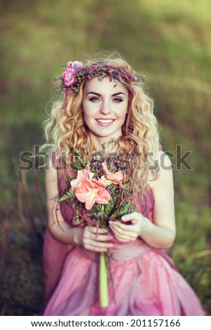 Portrait of a beautiful blonde girl in a pink dress with long developing a bouquet of flowers in their hands