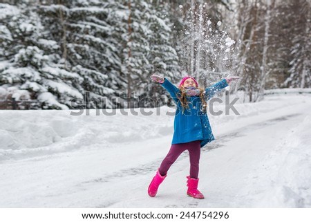 Six year old girl dressed in a blue coat and a pink hat and boots throws snow up