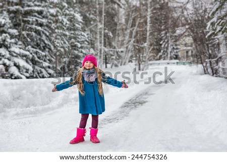 Cute six year old girl dressed in a blue coat and a pink hat and boots, hamming and playing in the winter forest
