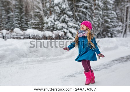Cute six year old girl dressed in a blue coat and a pink hat and boots, fun runs through the winter forest
