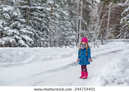 Cute six year old girl dressed in a blue coat and a pink hat and boots throws snow and laughs