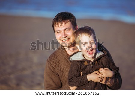 A young dark-haired man is smiling and embracing his five-year-old laughing son. Clothes: casual.