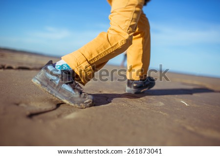 The close-up of the legs of a boy running along the beach. Clothes: yellow pants, trainers.