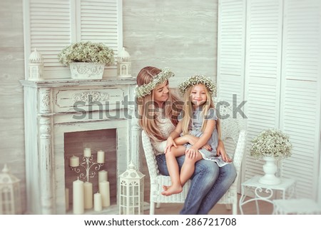 ? happy mother is kissing the hand of her young daughter. They are sitting in the armchair.They are having casual clothes and floral wreathes on. The atmosphere of happiness is all around them.