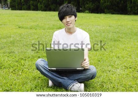 Young male university student sitting on the grass working on laptop at campus