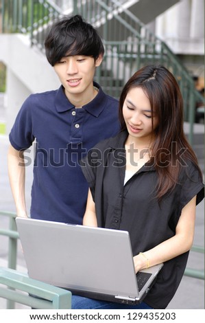 Asian college couple student holding laptop on campus