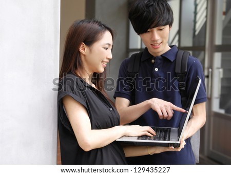 Asian college couple student sitting holding laptop on campus