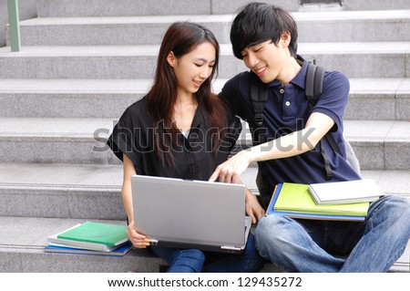 Couple college friends sitting holding laptop with books on campus