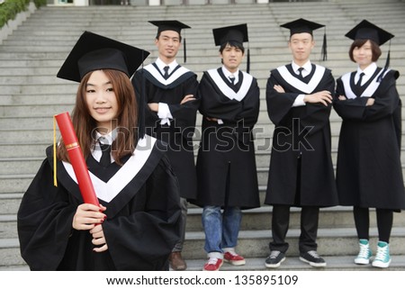 Group of graduation students with diplomas outdoors- female graduate wearing a graduation gown