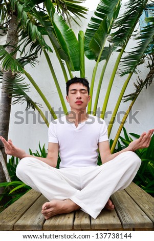 A young man doing yoga in Nature sitting wooden chair