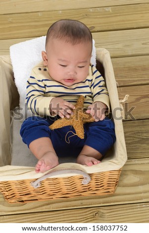 Asian Adorable laughing baby holding starfish sitting in a laundry basket on wooden floor