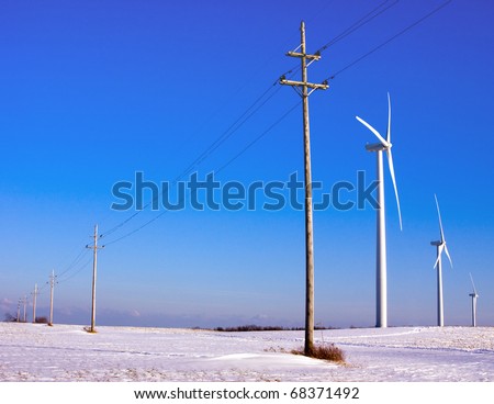 Concept picture of environmental friendly source of power. Power lines on wooden poles fading in the horizon; three windmills on the right third of the picture.