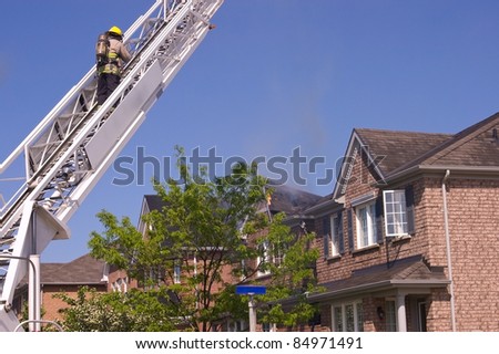 Firefighter wearing a self contained breathing apparatus on an engine ladder surveys an extinguished fire that damaged a roof top.