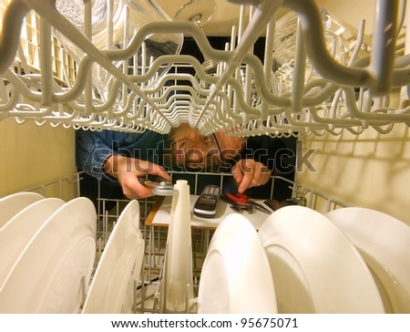 Frustrated grimacing service technician trying to fix a dish washer. Horizontal picture from inside the machine.